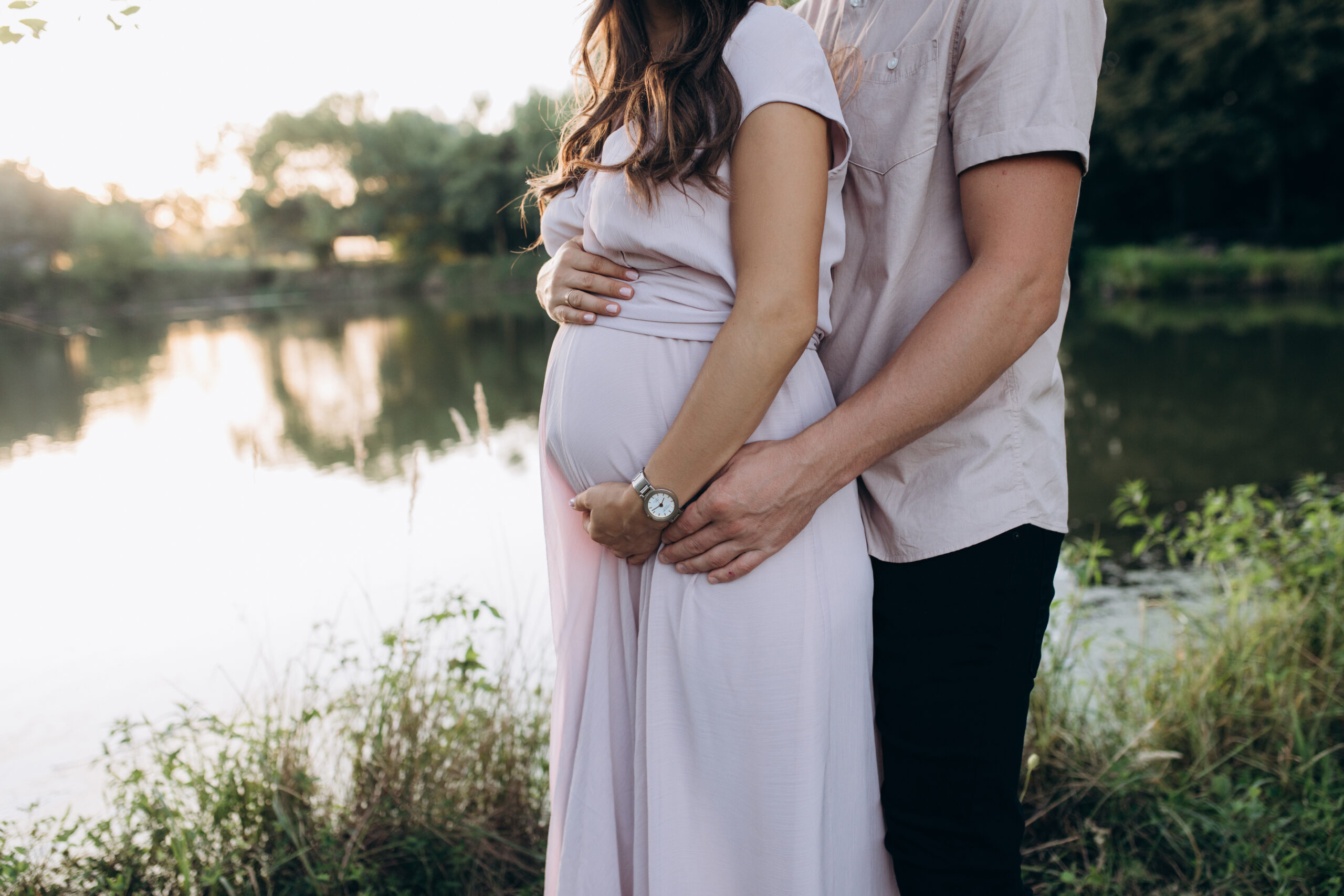 Man hugs beautiful pregnant woman tender standing before the lak